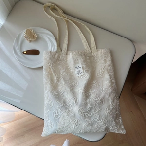 Detailed close-up of beige lace floral embroidery and logo patch on cotton tote bag
