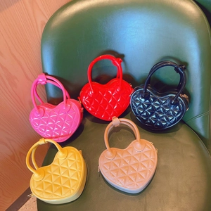 Five colorful heart-shaped quilted handbags displayed on a green leather chair