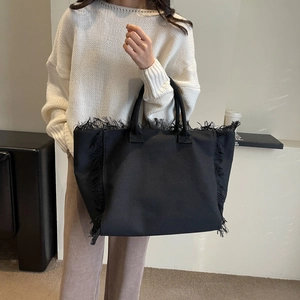 Minimalist black canvas tote bag with decorative fringe details shown in a lifestyle setting