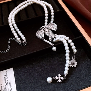 Detailed view of vintage double-layer pearl necklace with silver wing and cross charms