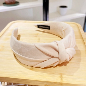 Detail of cream fabric knotted headband featuring a Hand Made woven label on a wooden tray