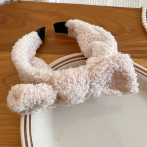 Close-up of beige plush bow headband with soft lamb wool texture on elegant white plate