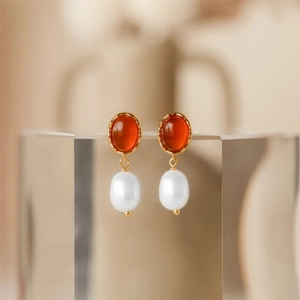 Detailed macro shot of vintage gold earrings with red oval gemstones and hanging white pearls