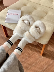 Close-up of cozy off-white plush slippers and striped wool socks on warm wood floor