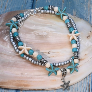 Detail of bohemian layered anklet with starfish pendants and turquoise beads on a shell