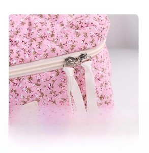 Close-up of double metal zippers and woven pulls on floral quilted cosmetic bag