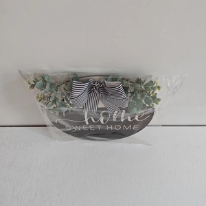 Detail of home SWEET HOME oval wood sign with striped bow and eucalyptus leaves in packaging
