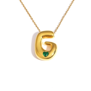 Macro detail of 18k gold plated bubble letter G pendant with green heart gemstone