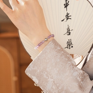Detail of amethyst beaded bracelet with silver charm worn against a traditional fan