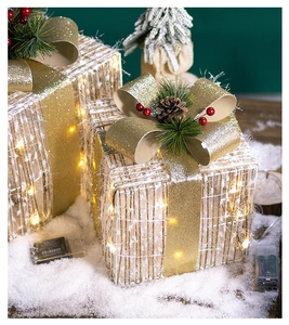 Close-up of glowing white wire Christmas gift boxes with pine cones and golden bows