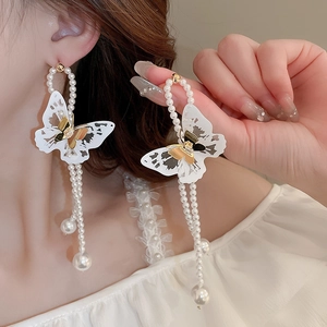 Detail of white butterfly pearl tassel earrings with golden finish worn by model