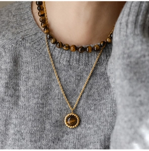 Detail of layered tiger eye beaded necklace with a golden pendant on a model wearing knitwear