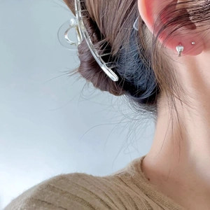 Detailed view of silver heart stud earrings and transparent hair claw clip worn by a model