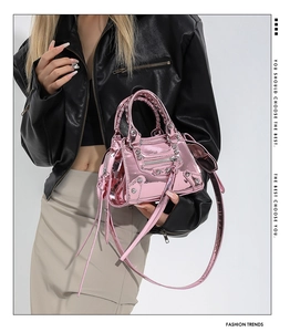 Detail of metallic pink patent handbag with studs, braided handle and long tassels