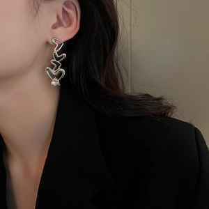 Detail of silver drop earrings with layered hearts and a pink teardrop crystal on a model