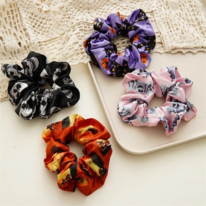 Macro view of four Halloween satin hair scrunchies with skull, pumpkin, and ghost prints