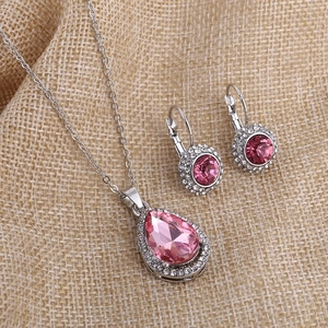 Pink crystal waterdrop necklace and moon earrings set on brown linen background