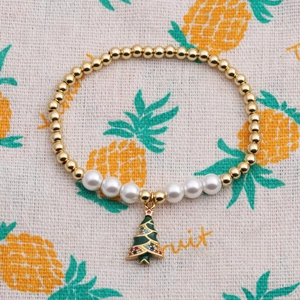 Détail d'un bracelet doré avec perle blanche et un pendentif de sapin de Noël coloré