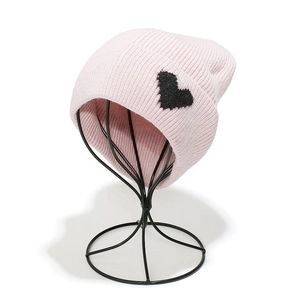 Detail of pink knitted beanie with black velvet heart patch on a black metal hat stand