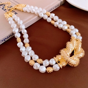 Detail of double-layer baroque pearl necklace with a large golden knot-shaped charm