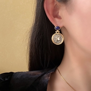 Close-up of vintage coin earrings with blue gemstone and silver pin on female model