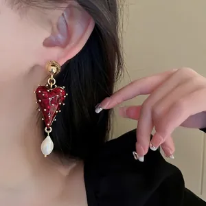 Boucles d'oreilles cœur rouge vintage avec clous dorés et perle sur modèle
