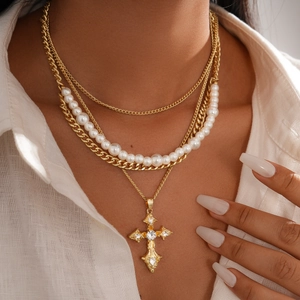 Close-up of layered gold necklace with faux pearls and a crystal-set cross pendant