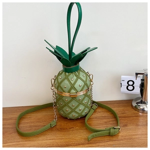Detail view of the green pineapple crossbody bag with gold stud accents on wood