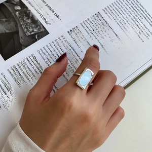 Detail of silver rectangular shell ring worn on finger with fashion magazine backdrop