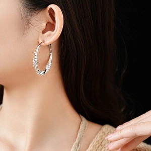 Close-up of silver twist hoop earrings with sparkling rhinestones worn by a model