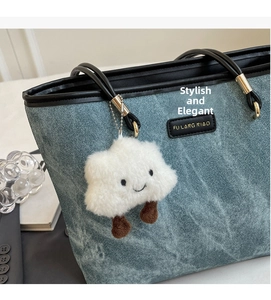 Close-up of fluffy white cloud plush keychain accessory on a blue denim shoulder bag