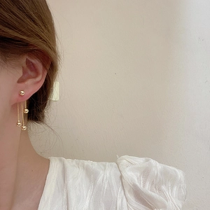 Detail of gold tassel earrings with metal balls worn by a model in soft lighting