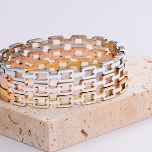 Minimalistische rechteckige Armreifen in Gold, Roségold und Silber auf Steinpodest