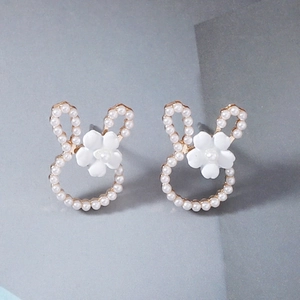 Detailed close-up of cute golden bunny stud earrings with white pearls and small flowers