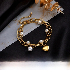 Close-up of golden double-layer chain bracelet with white pearls and heart pendant