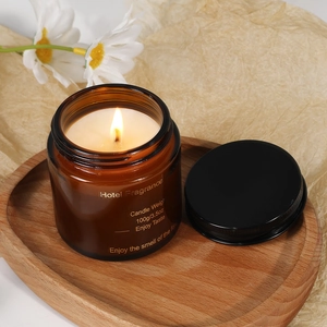 A 100g amber glass jar scented candle on a wooden tray with white daisies