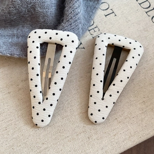 Dettaglio di due fermagli per capelli a triangolo in tessuto con classici pois neri