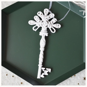 Close-up of vintage resin key ornament with white silk ribbon in a dark green tray