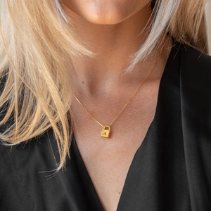Close-up of golden necklace featuring a padlock pendant engraved with letter A on a model