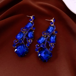 Close-up of gold dangle earrings with blue crystal clusters on dark satin background