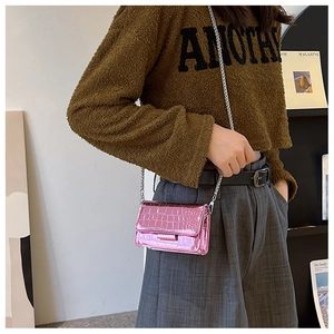 Detail of pink faux crocodile leather mini bag with chain strap worn by a model