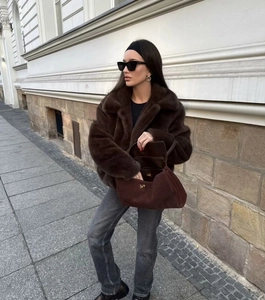 Detailed texture of brown faux fur jacket paired with a suede handbag in outdoor street style