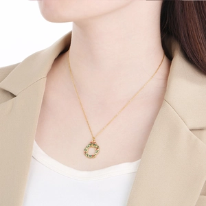 Elegant gold Christmas wreath necklace with red and green accents worn by a female model