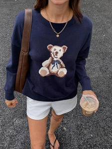 Flat lay of navy knit sweater featuring a brown teddy bear motif with white shorts