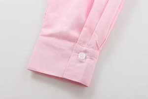 Detail view of pink cotton shirt cuff featuring a white translucent button and fine stitching