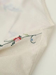 Détail de broderie florale et bords ourlés sur surface en coton et lin beige clair