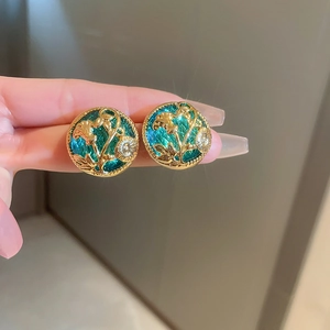 Close-up of vintage round gold earrings with green floral enamel inlay details