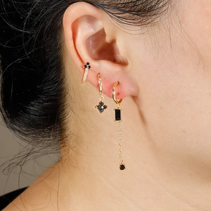 Detail of gold zircon earring set featuring black stones and layered chain style on model