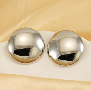 Vue détaillée de boucles d'oreilles rondes en argent poli sur fond de soie dorée