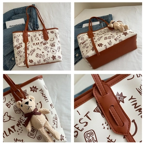 Close-up of brown and white tote bag with graffiti prints, stitching, and bear charm